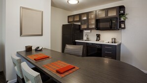A compact kitchen with dark cabinetry, a microwave, and a refrigerator. There is a dining table with two chairs and orange placemats. - Candlewood Suites Austin-Round Rock by IHG (Round Rock)