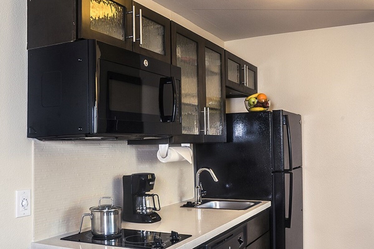 A compact kitchen with black appliances, a coffee maker, and a fruit bowl on the counter.
