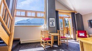 A room with large windows, wooden furniture, and a view of mountains. - Brewster Mountain Lodge (Banff)
