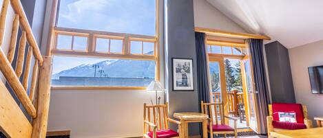 A room with large windows, wooden furniture, and a view of mountains.