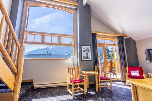 A room with large windows, wooden furniture, and a view of mountains. - Brewster Mountain Lodge (Banff)