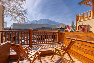 Una terraza de madera con dos sillas, vista a una montaña y un edificio con el letrero 'MAGPIE & STUMP RESTAURA'.