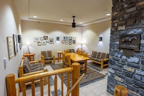 A room with a wooden dining table, chairs, a sofa, and a stone wall with a mounted sculpture.