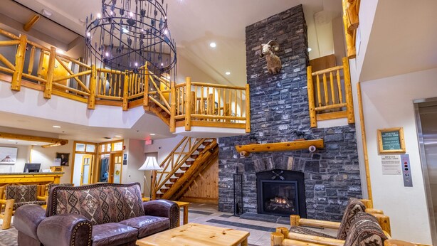 A spacious lobby with a fireplace, wooden furniture, and a staircase leading to an upper level. - Brewster Mountain Lodge (Banff)