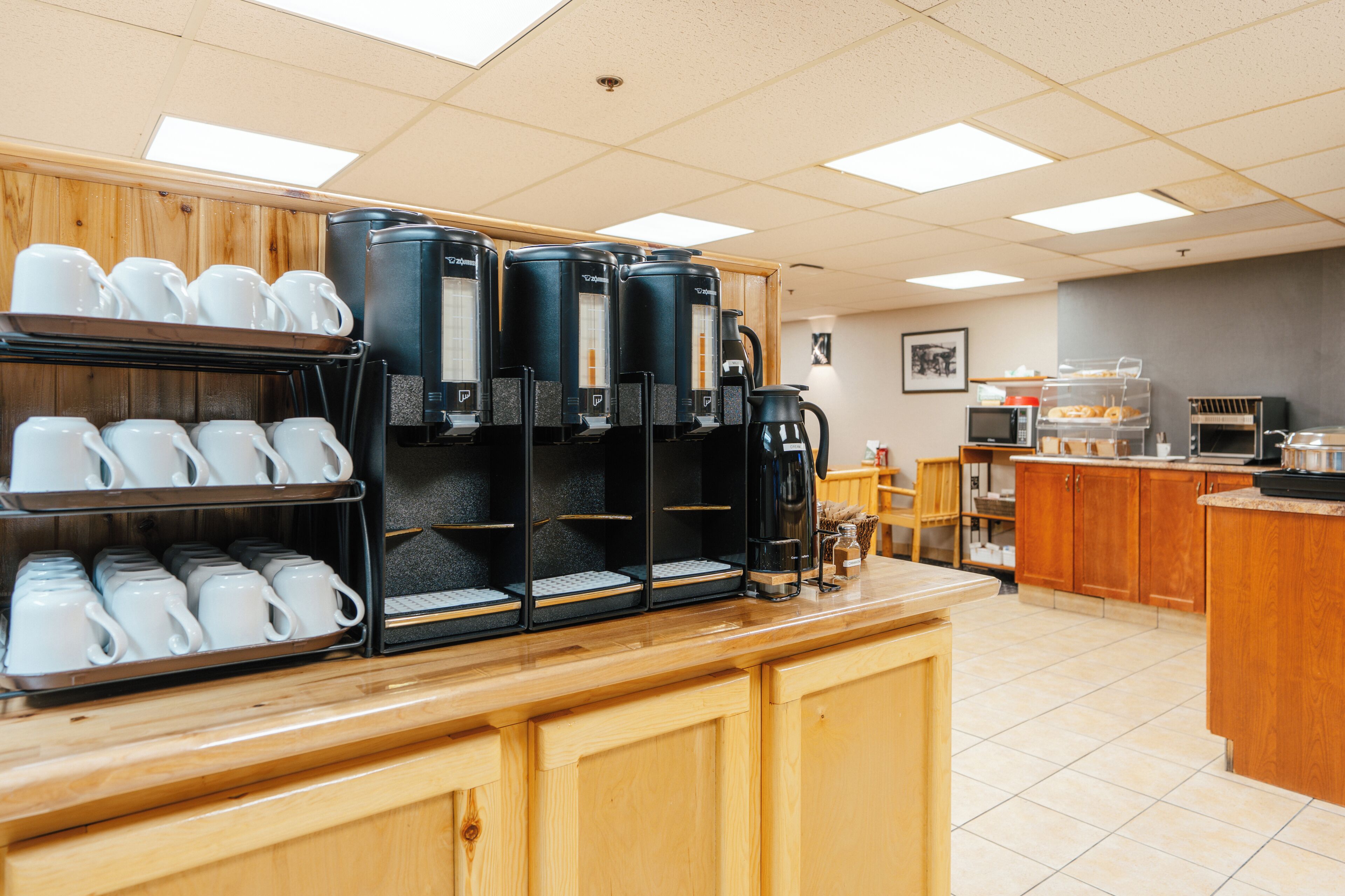A coffee station with multiple coffee makers and a display of white cups.