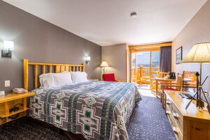 A hotel room with a bed, a desk, a chair, a lamp, and a view of the outside.