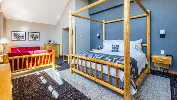 A room with a four-poster bed, a red sofa, a desk, and a lamp.