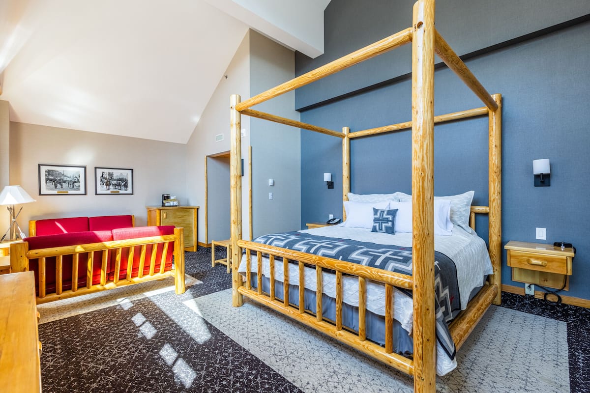 A room with a four-poster bed, a red sofa, a desk, and a lamp.