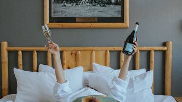 A person lying in bed with a bottle and glass of wine, a framed photo on the wall, and a wooden headboard.