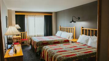 A hotel room with two beds, a desk with a lamp, a chair, and a window with curtains.