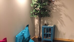 A room with a patterned carpet, a blue side table, a potted plant, and a pink and blue bag. - Brewster Mountain Lodge (Banff)