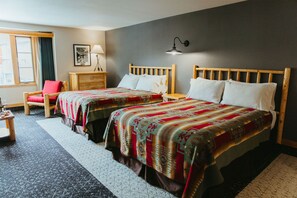 Habitación de hotel con dos camas, cabecero de madera, una silla roja, cómoda de madera y una ventana con cortinas.