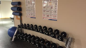 A gym with a wall-mounted dumbbell rack and exercise posters.