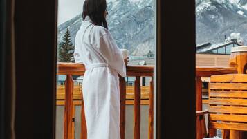 A person in a white robe standing on a balcony with wooden railings, overlooking a mountainous landscape.