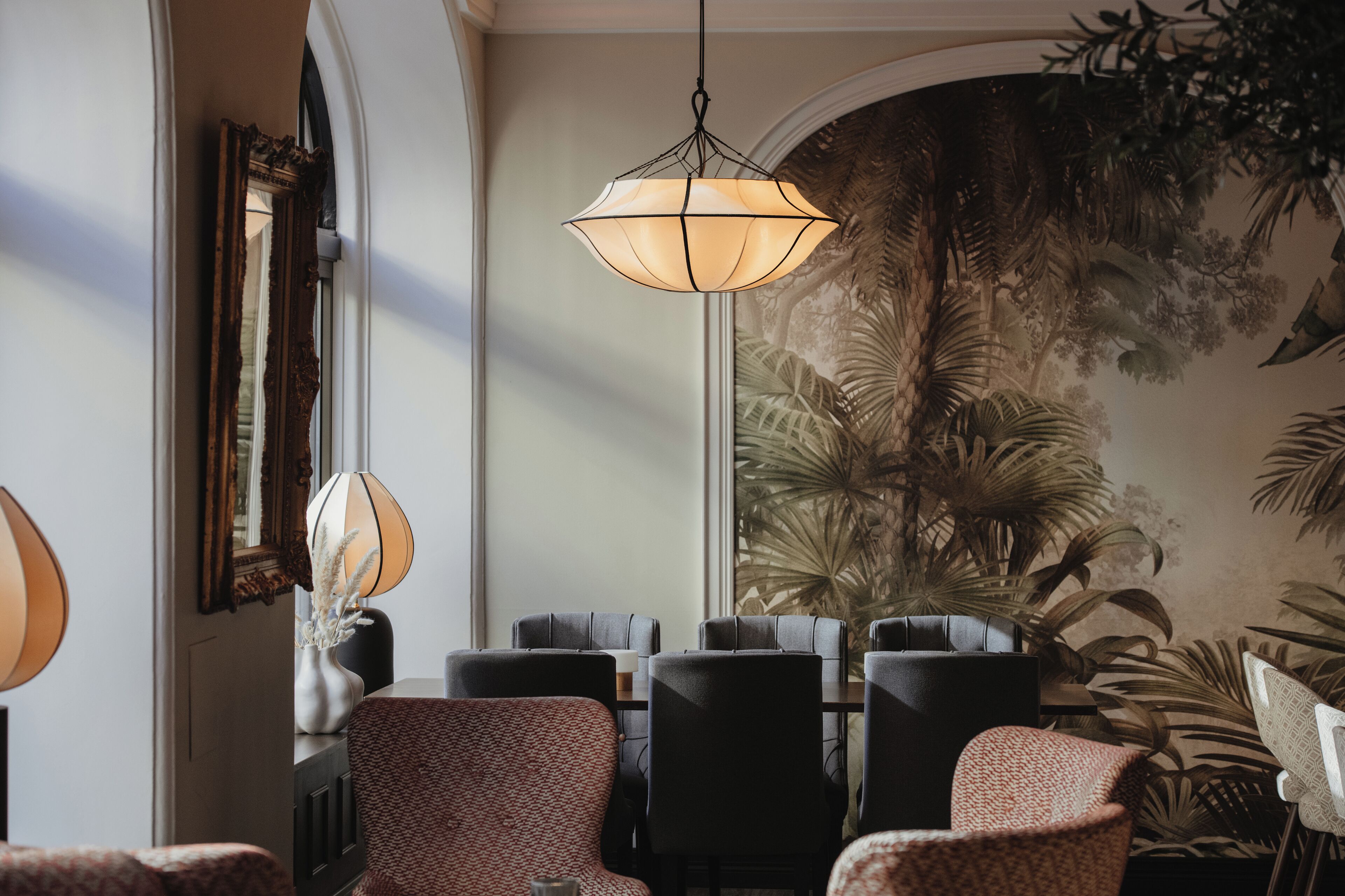 A dining area with a chandelier, chairs, and a mural of tropical foliage.