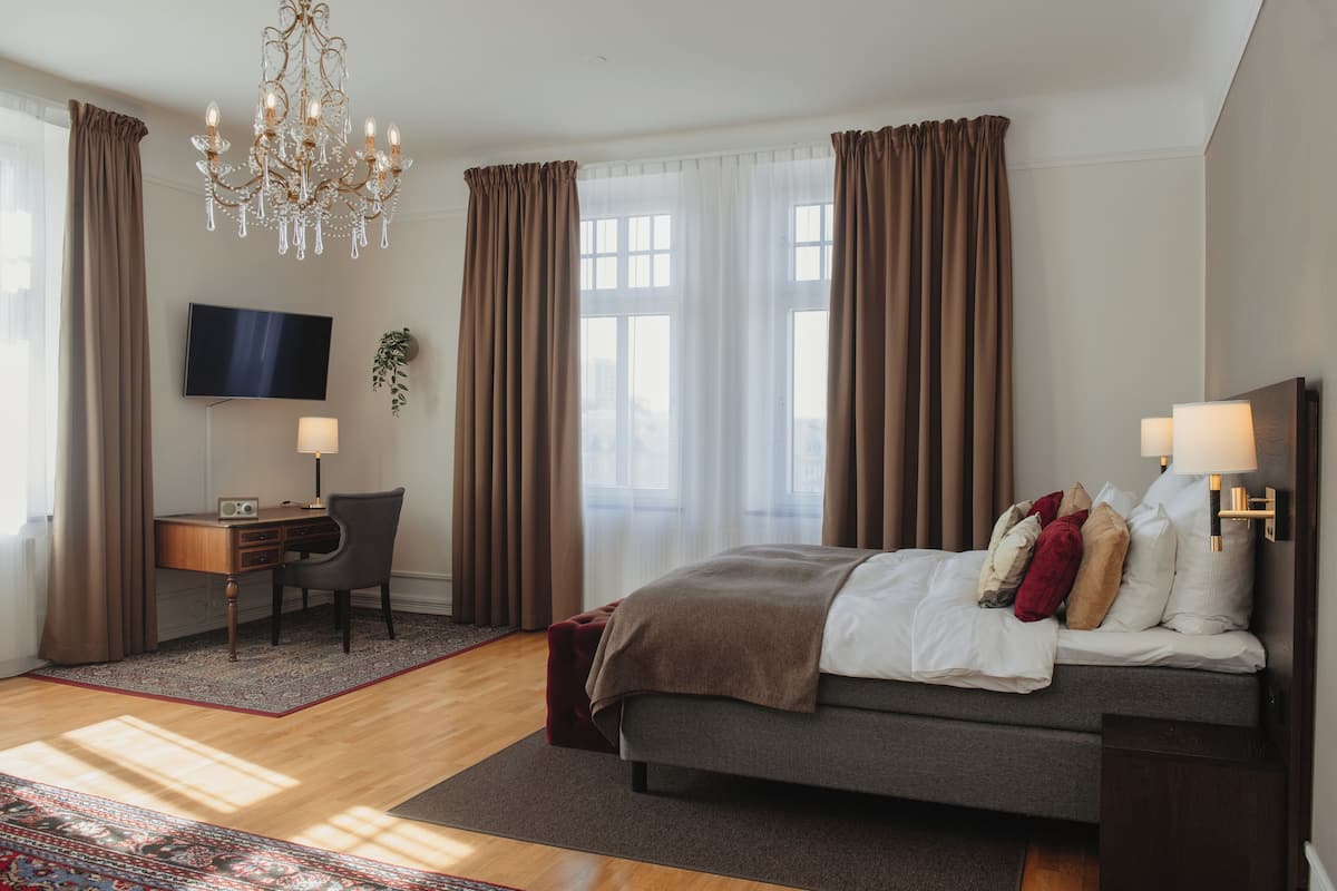 Quarto de hotel moderno com cama, escrivaninha, cadeira e televisão.