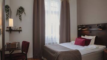 A hotel room with a bed, a desk, a chair, a nightstand, a lamp, and a window with curtains.