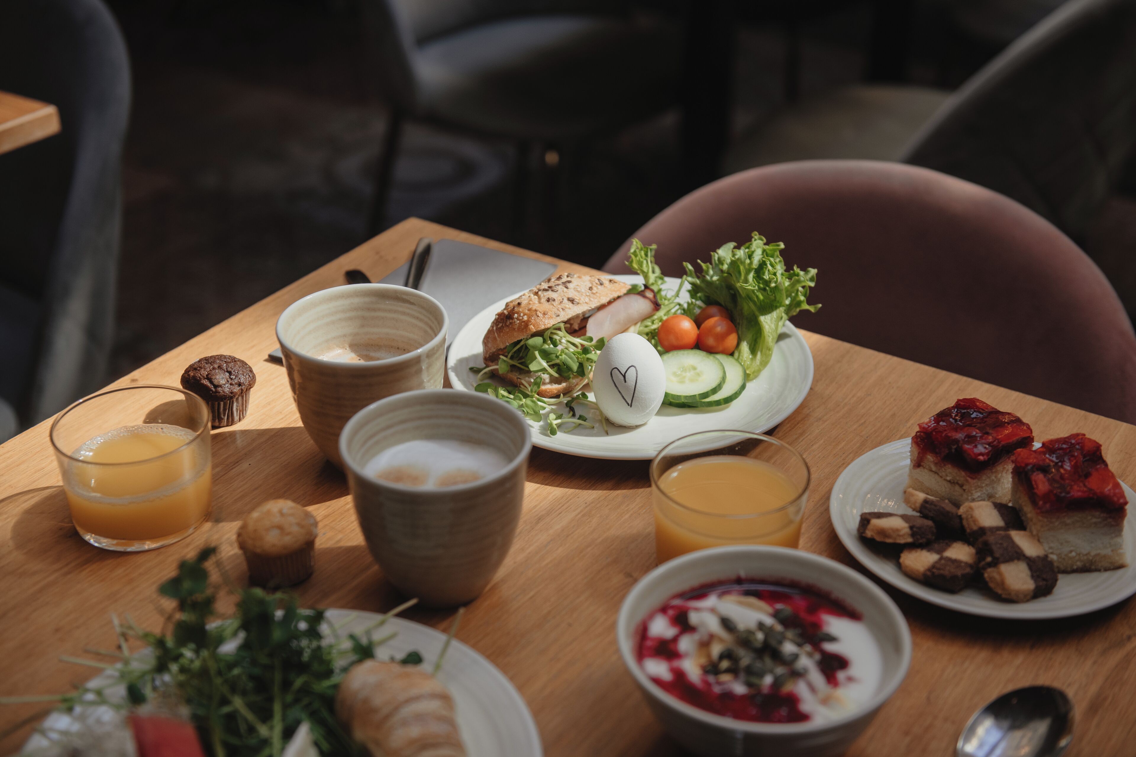 Una mesa de desayuno con diversos alimentos, entre ellos pan, huevos, verduras y un postre.