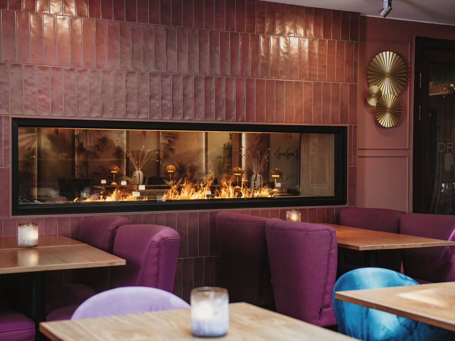 A restaurant with a large window overlooking a fire, purple seating, and decorative wall panels.