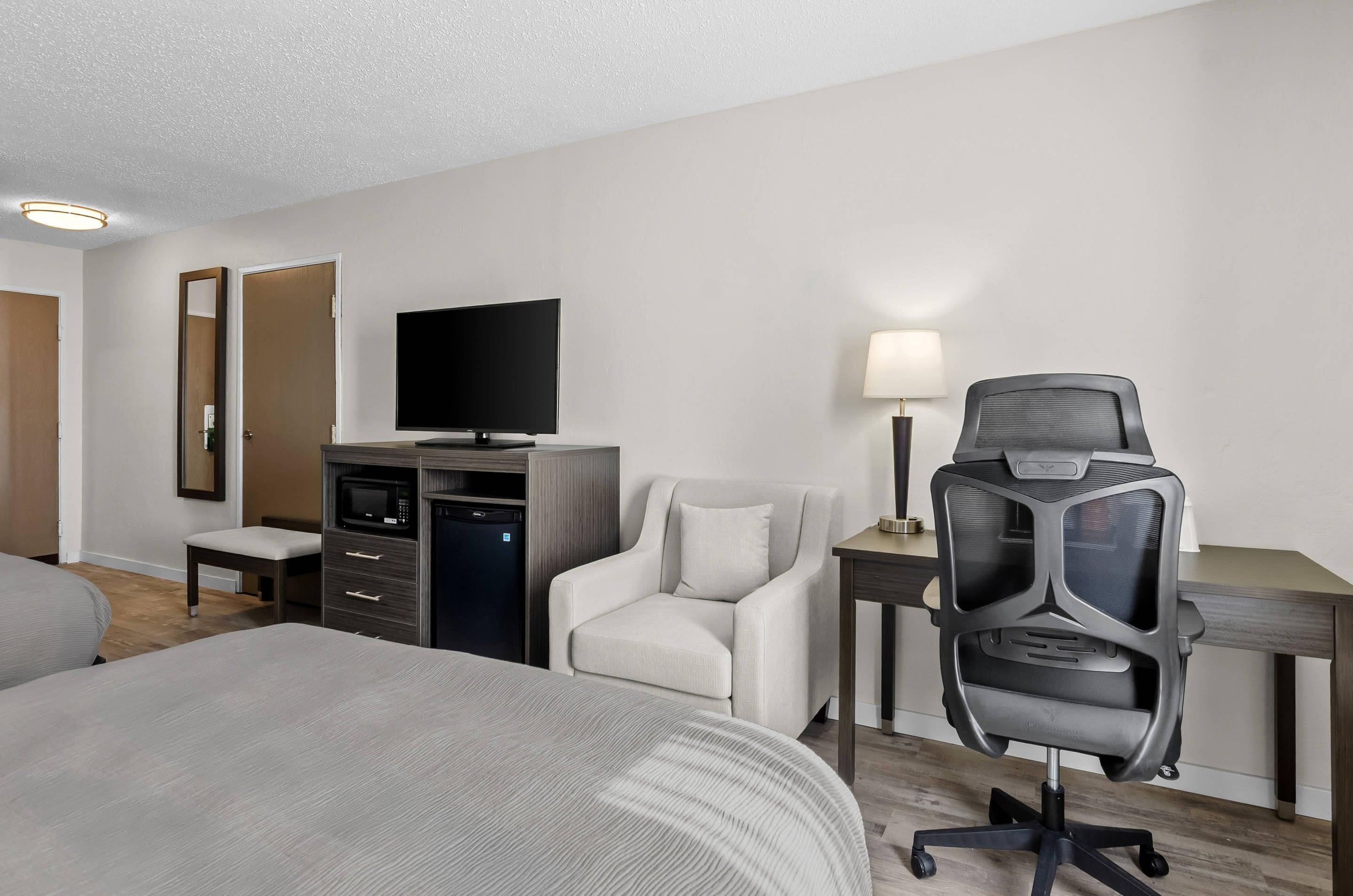 Quarto de hotel com uma cama, escrivaninha com computador, cadeira, televisão e micro-ondas.