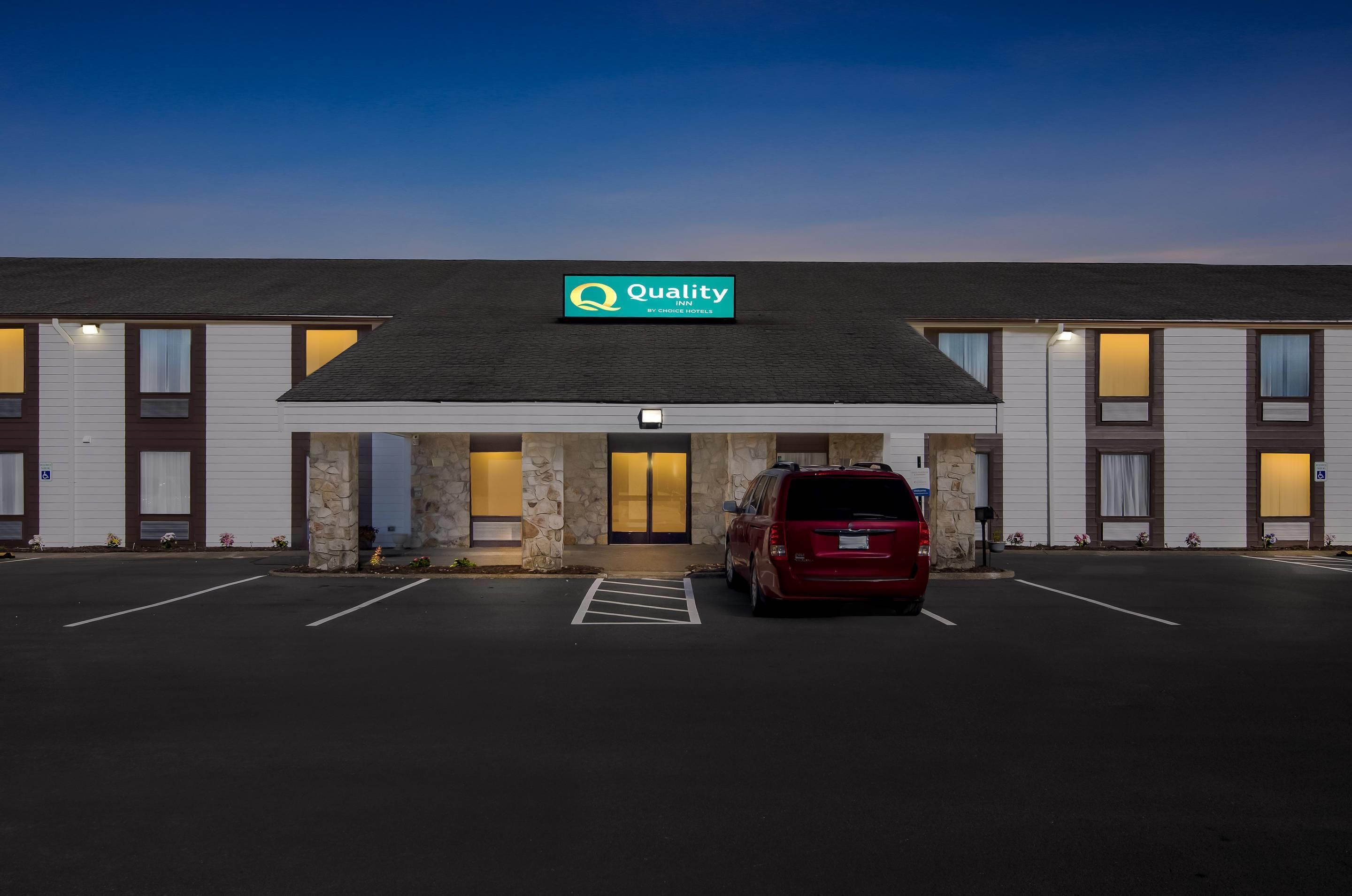 A hotel with a sign reading 'Quality by Choice Hotels' and a red vehicle parked in the parking lot.