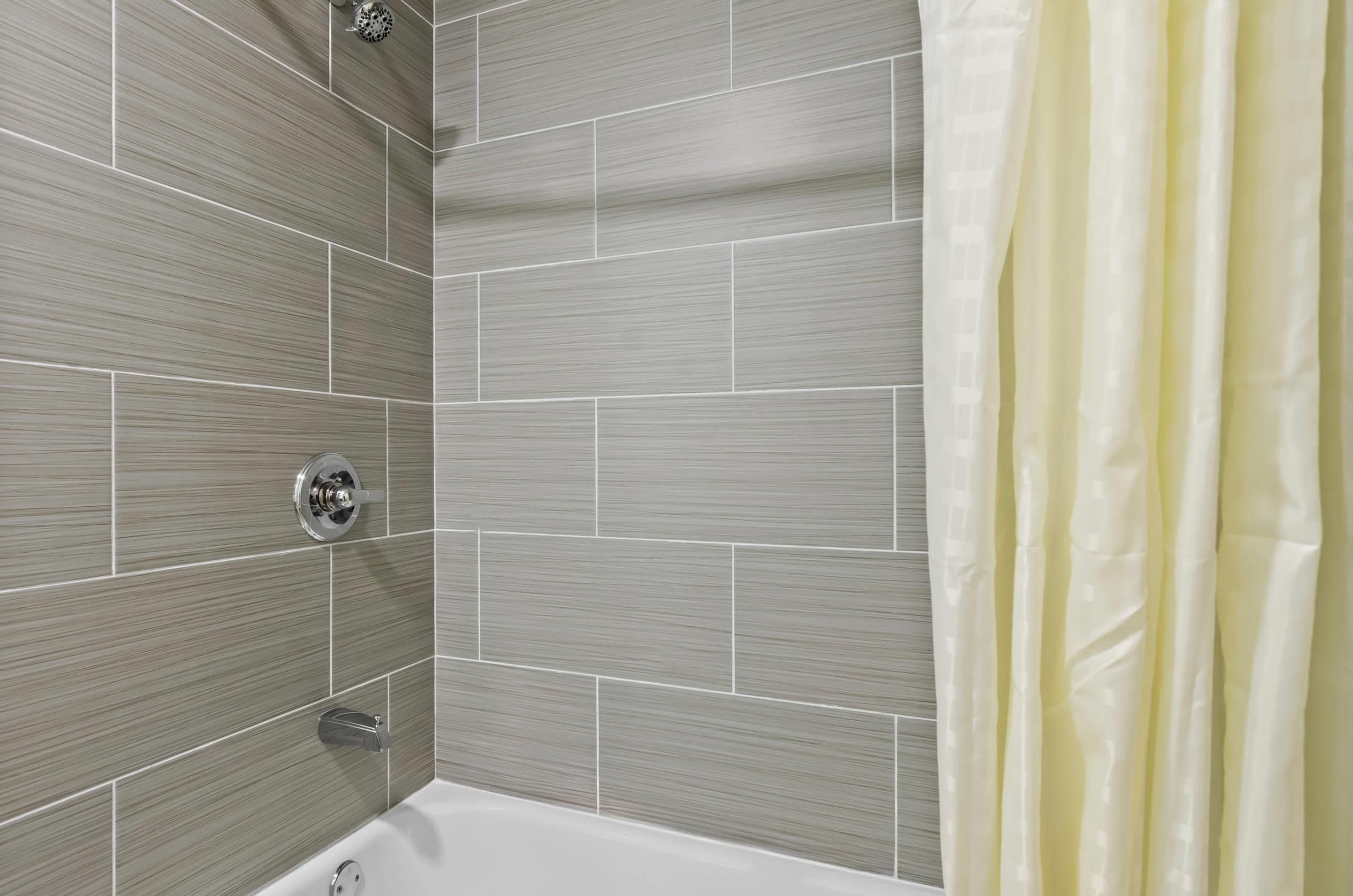Une salle de bain avec des murs carrelés de couleur grise, une baignoire blanche et un rideau de douche jaune.