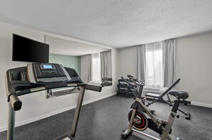 A gym with a treadmill, an elliptical, a TV, and a rack of dumbbells. - Quality Inn Ghent (Ghent)