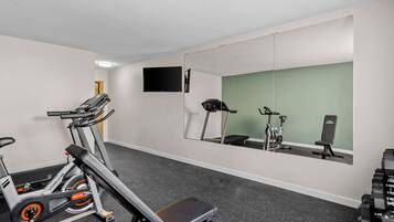 Uma academia com equipamentos de cardio, um banco e um espelho refletindo o ambiente.