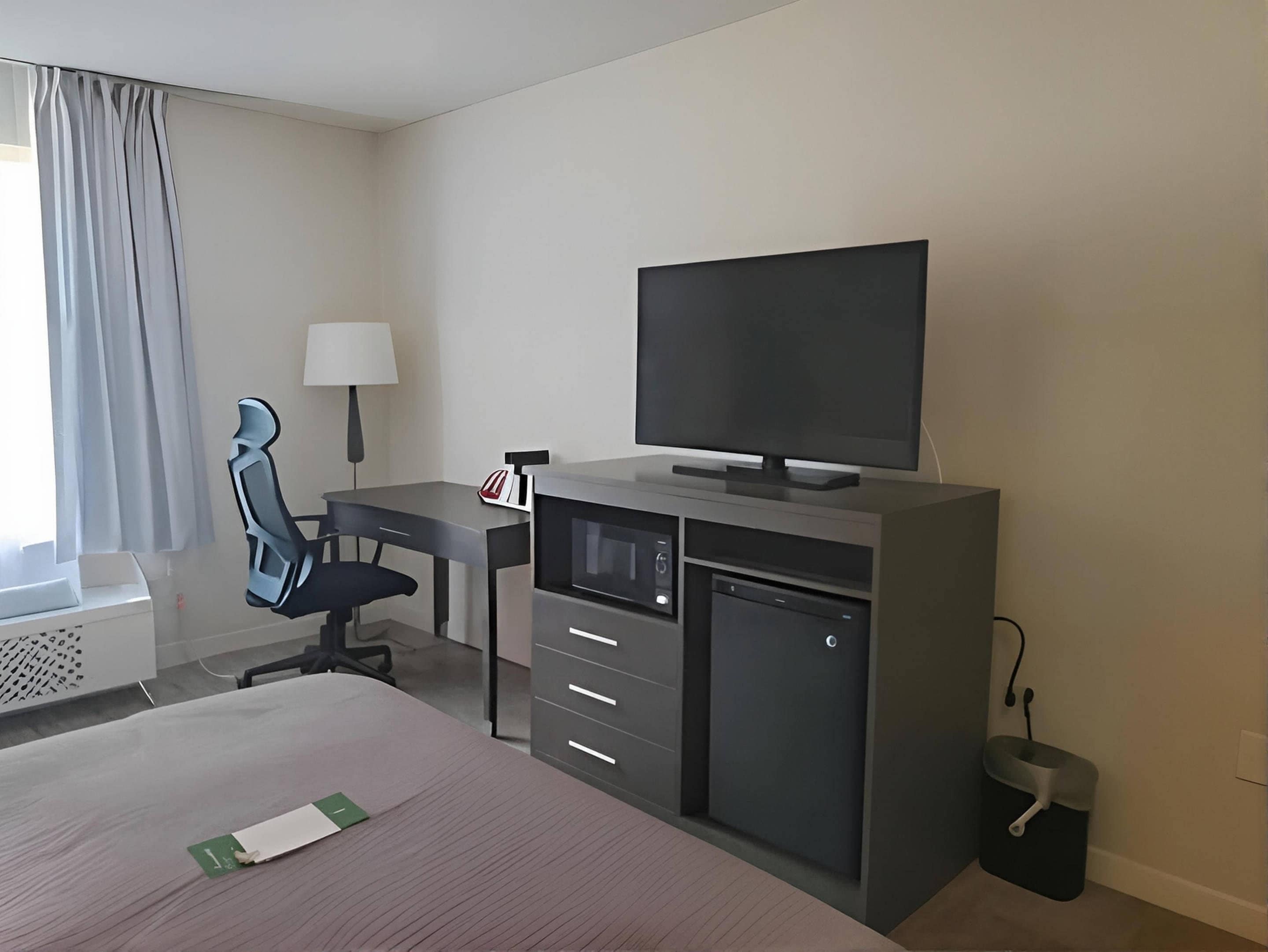 Una habitación de hotel con cama, escritorio, silla, televisor y una pequeña cocina.