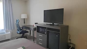 Una habitación de hotel con cama, escritorio, silla, televisor y una pequeña cocina.