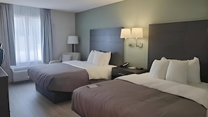 A hotel room with two beds, a bedside table with a lamp, a nightstand, and a window with curtains.
