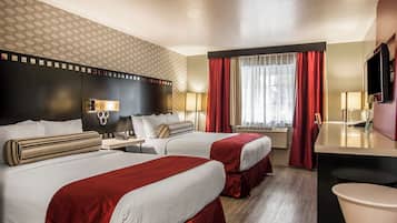 A hotel room with two beds, a desk, a TV, and a bathroom.