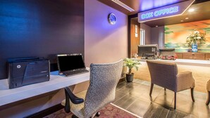 A hotel reception area with a desk, two chairs, a clock, and a sign reading "BOX OFFICE".