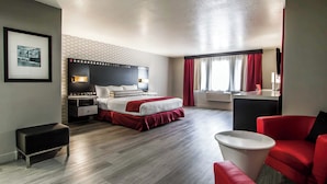 A modern hotel room with a large bed, a desk, a red chair, and a small table.