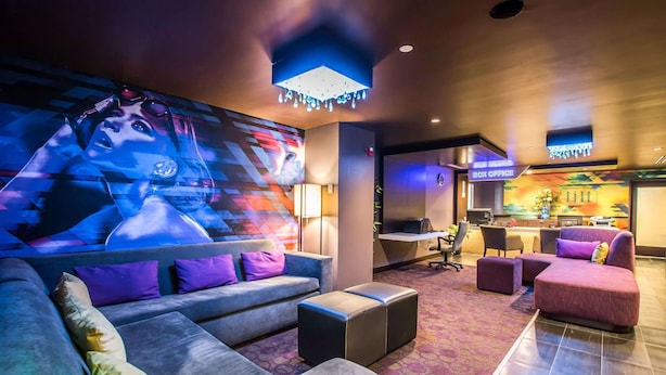 A modern hotel lobby with a large wall mural, plush seating, a reception desk, and a 'Box Office' sign.