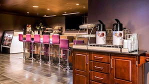 A bar area with purple bar stools, a coffee station with espresso machines, and a display of snacks.