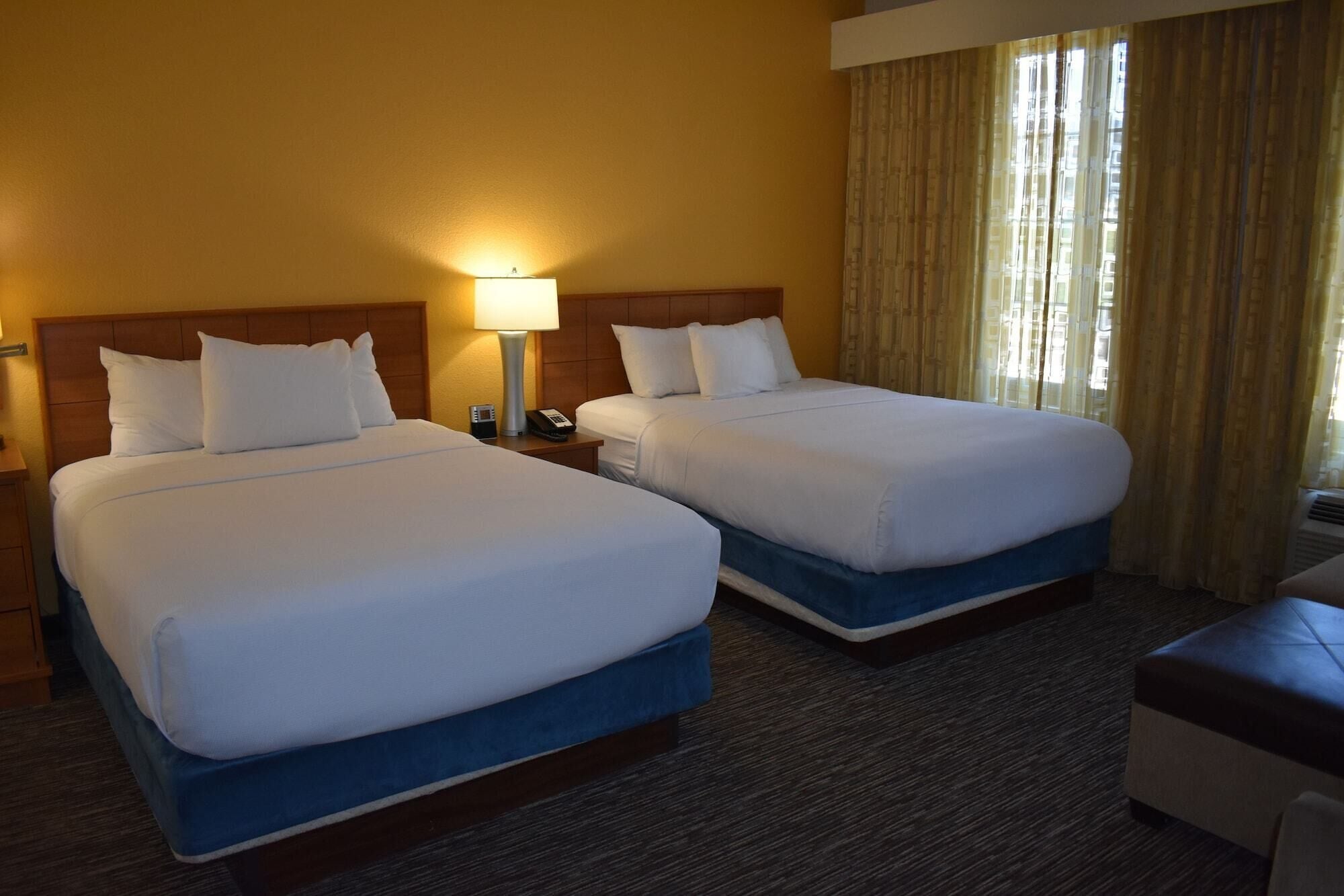 A hotel room with two beds, a nightstand with a lamp, a telephone, and a window with curtains.