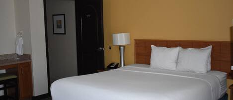 A hotel room with a bed, a nightstand, a lamp, a desk with a telephone, and a door.