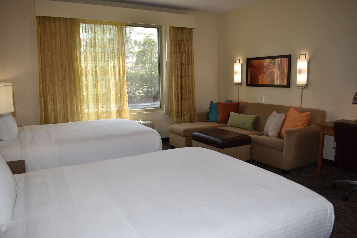 Hotellihuone, jossa on kaksi sänkyä, sohva, työpöytä ja ikkuna, jossa on verhot.