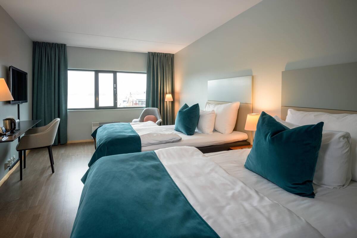 A hotel room with two beds, a desk, a chair, a TV, and a window with curtains.