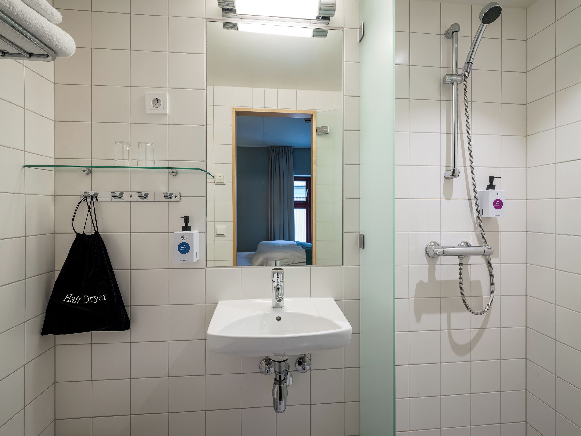 A bathroom with a sink, a glass shower enclosure, a hair dryer, and a mirror.