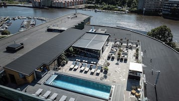 A rooftop pool area with lounge chairs and a swimming pool, surrounded by a parking lot and a body of water.
