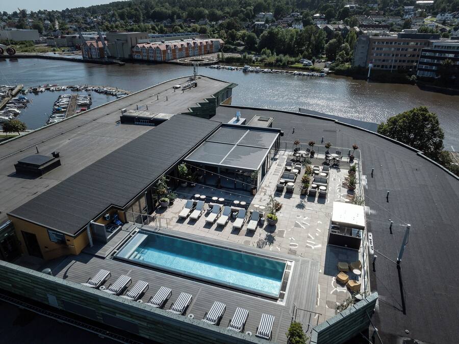 A rooftop pool area with lounge chairs and a swimming pool, surrounded by a parking lot and a body of water.