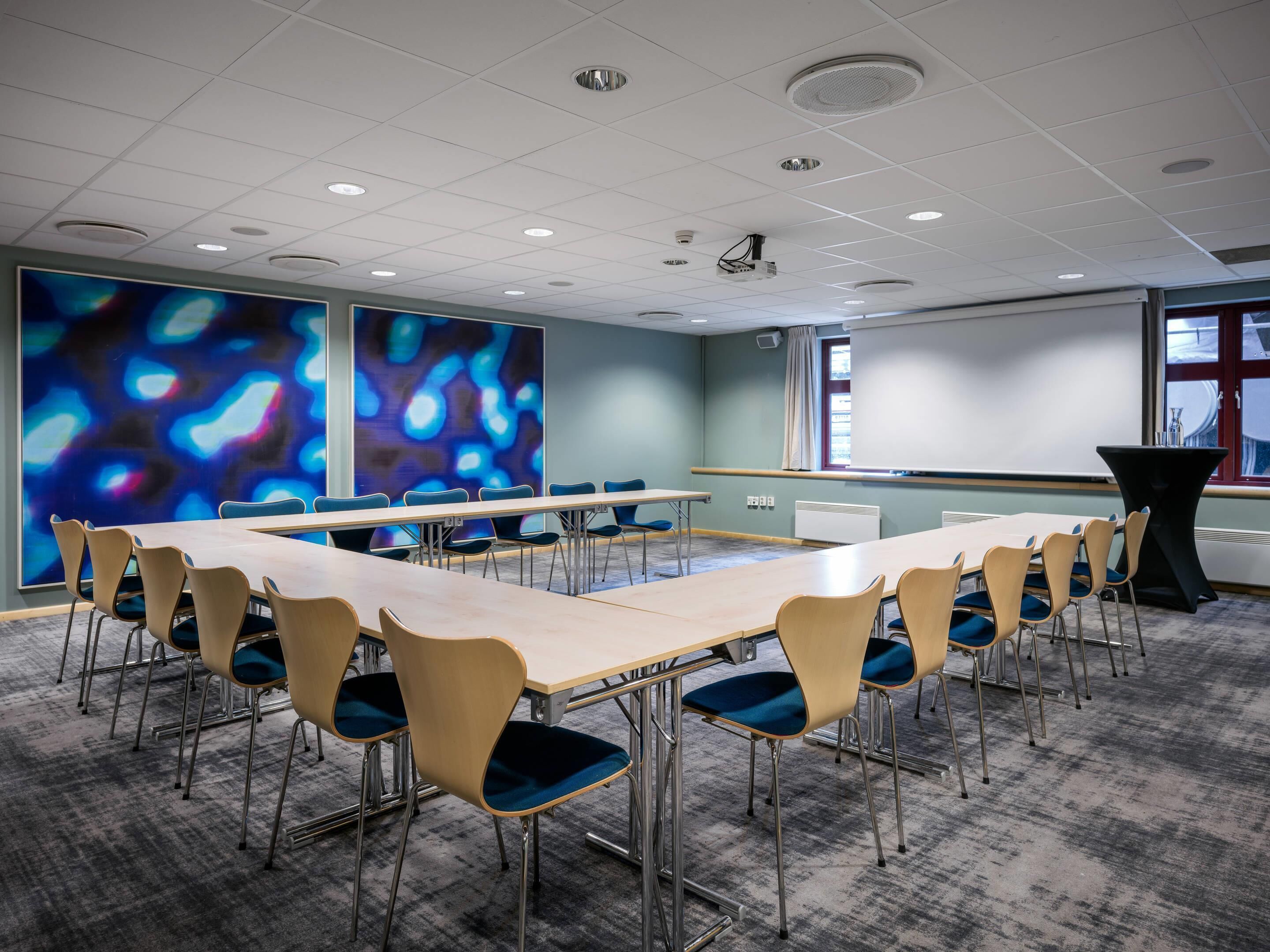 Una sala de conferencias con una gran mesa, sillas, un proyector y una pantalla.