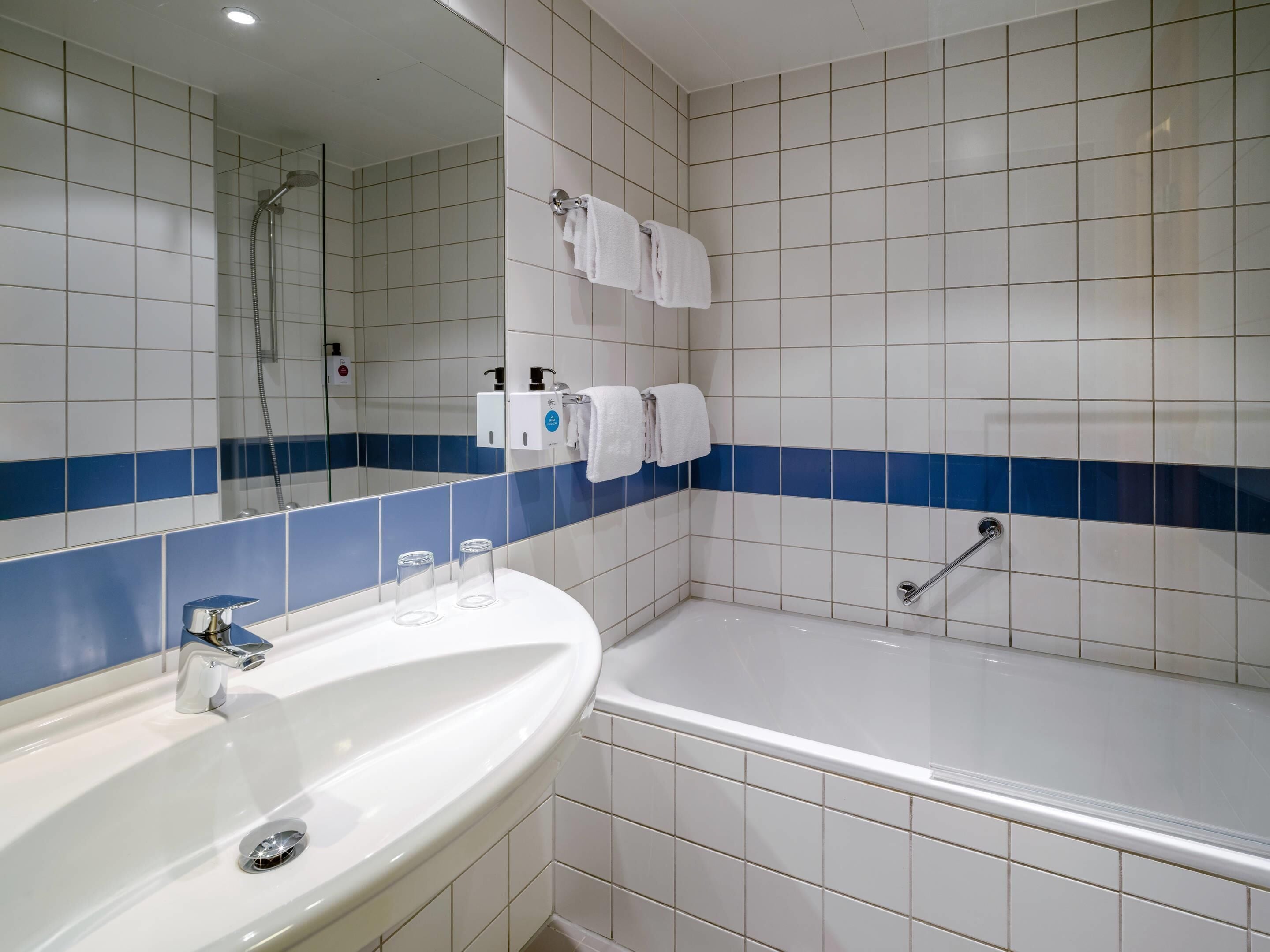 A bathroom with a white sink, a bathtub, and a shower. There are two towels hanging on the wall.