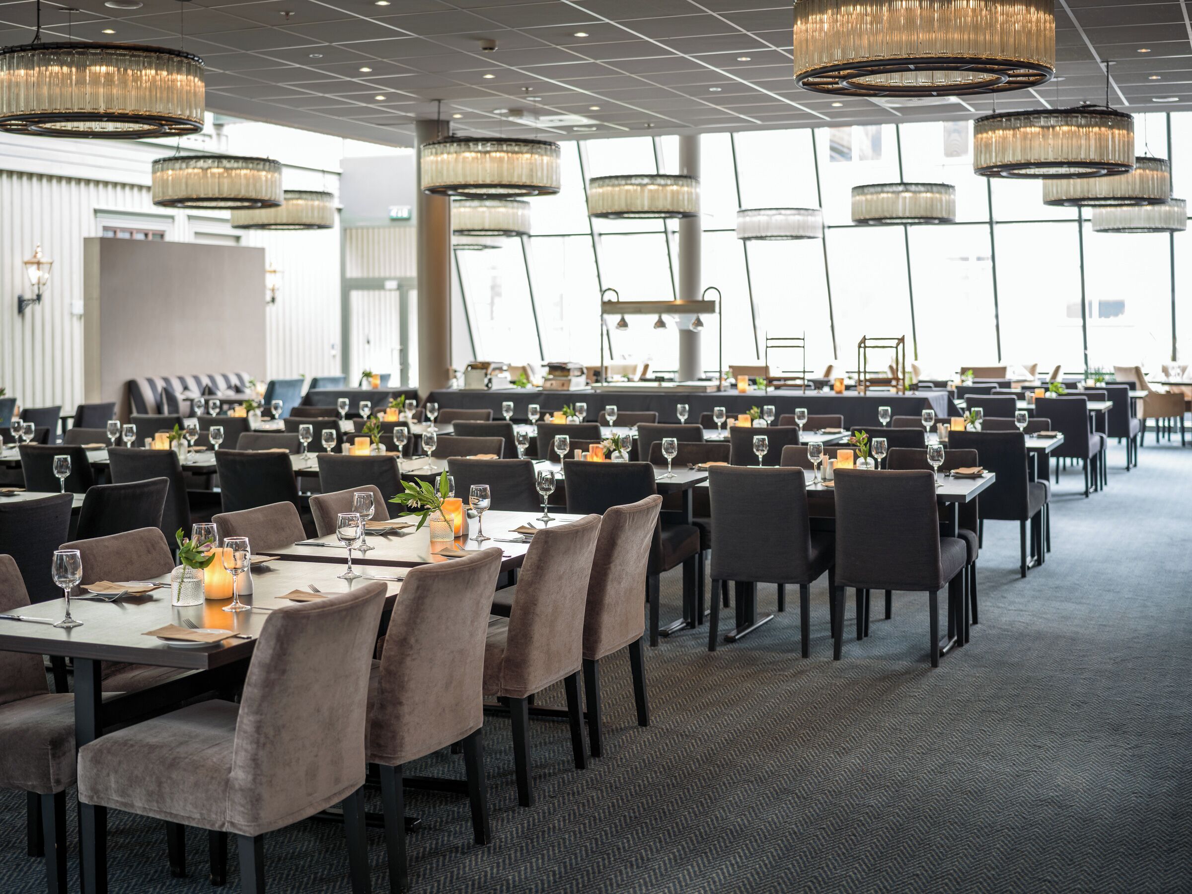 A spacious dining area with multiple tables, chairs, and elegant chandeliers.