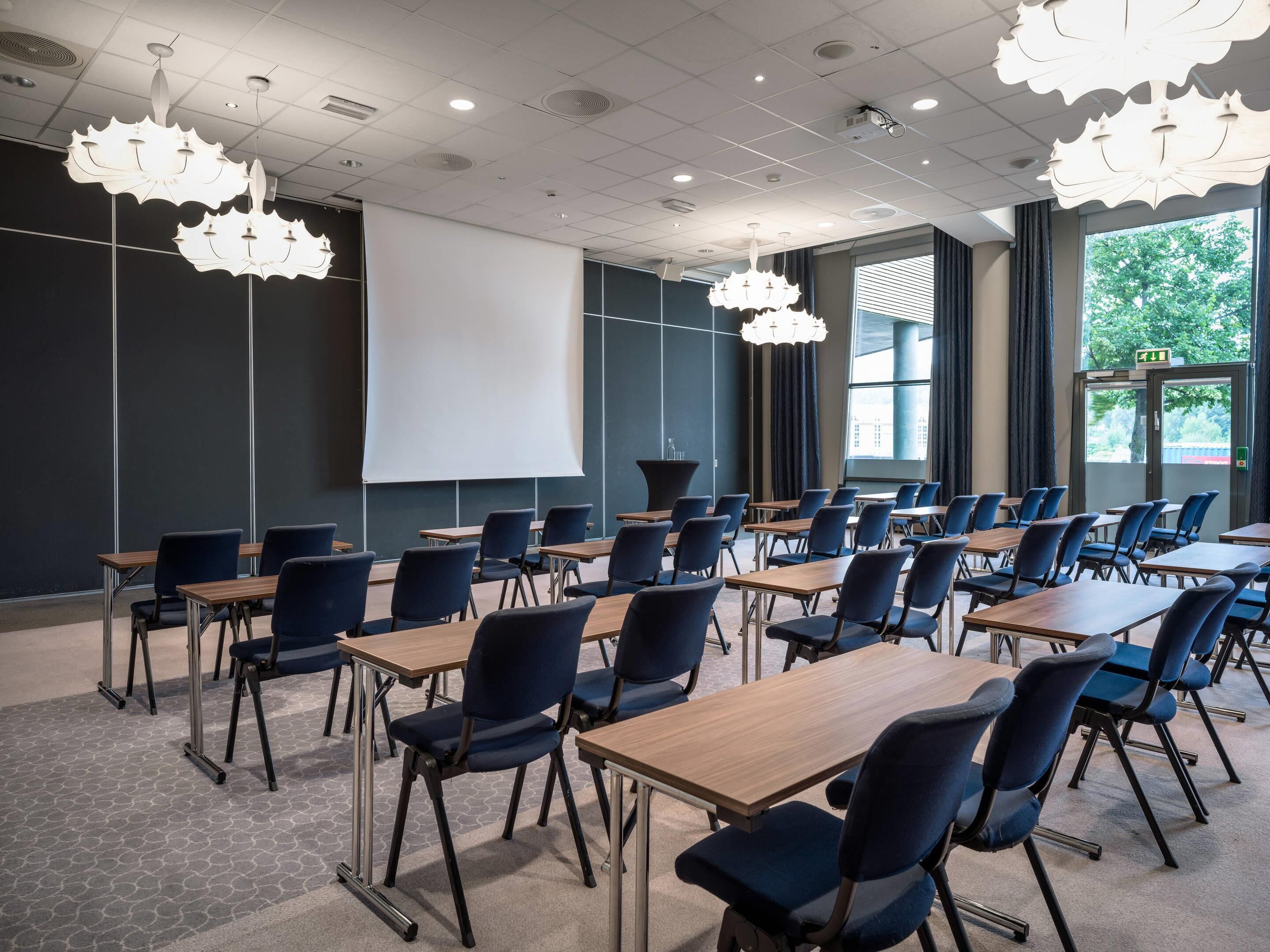 A conference room with tables and chairs, a projector screen, and large windows.