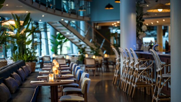 A modern indoor space with a long dining table, cushioned seating, and a staircase. - Quality Hotel Tonsberg (Tønsberg)