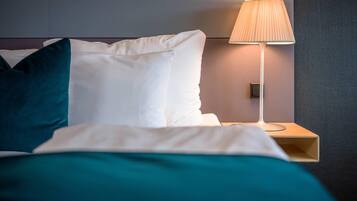 A neatly made bed with white and teal bedding, a bedside lamp, and a wall-mounted control panel.