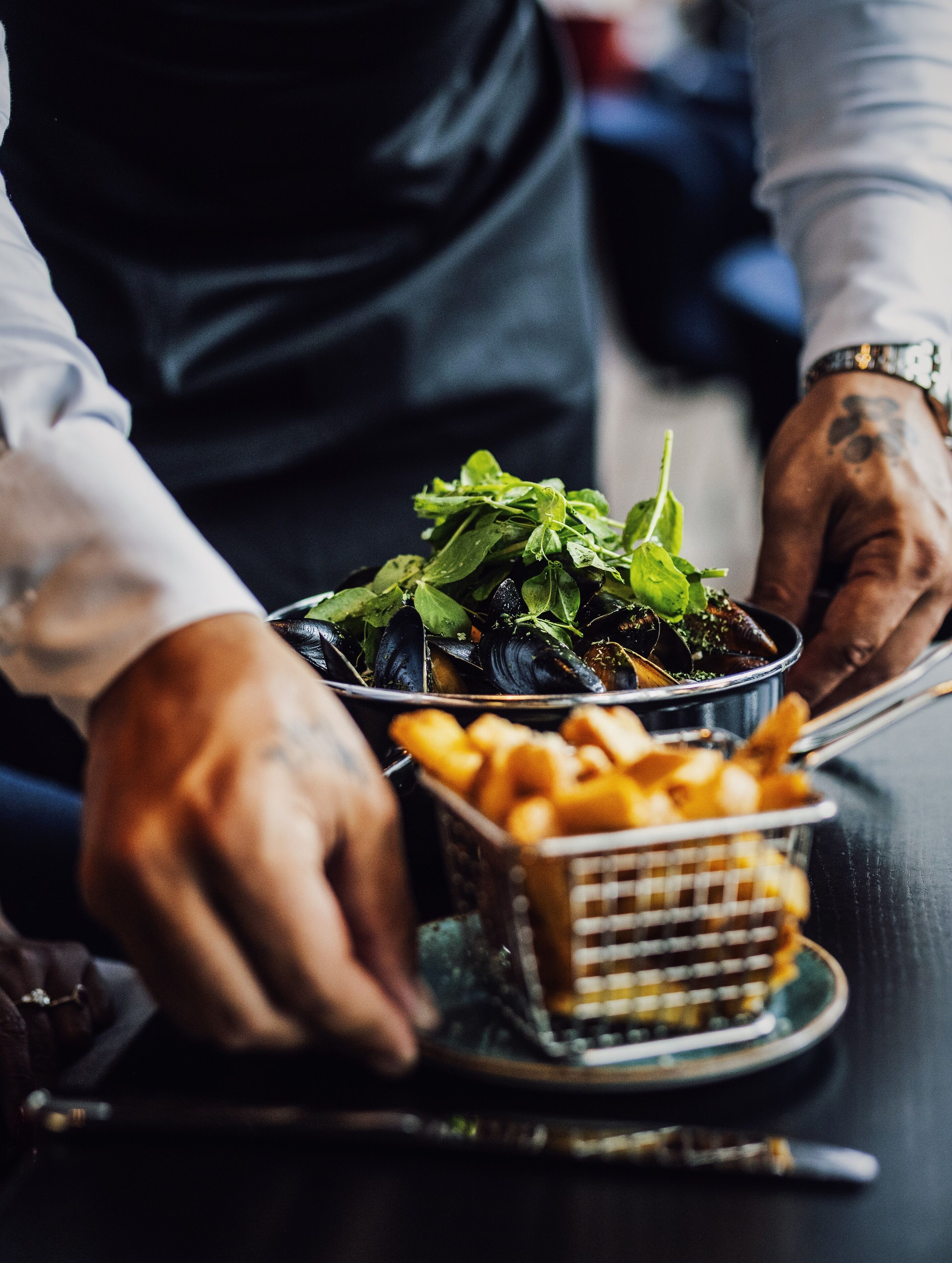 Una persona sirviendo comida, concretamente mejillones y papas fritas, sobre una mesa.